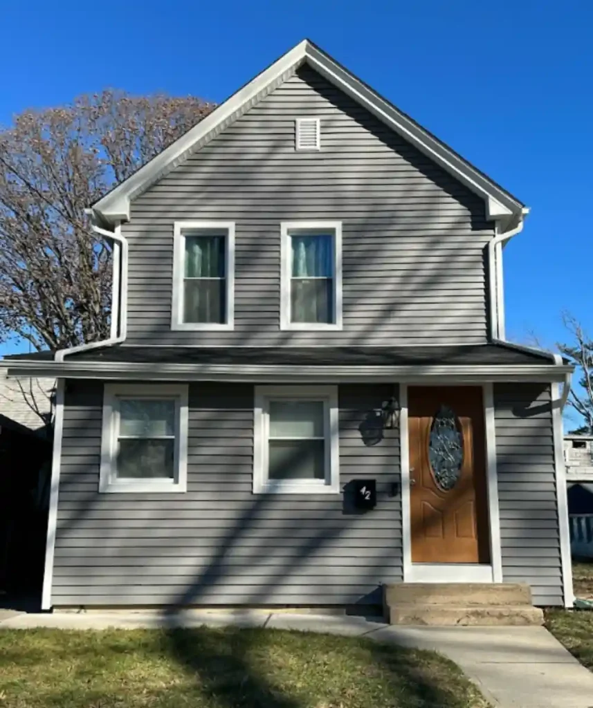 Updated vinyl siding on small two-story home under clear blue sky